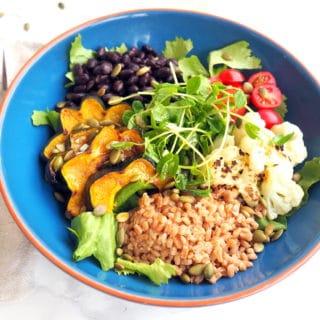 vegan power bowl featuring farro, roasted acorn squash, roasted cauliflower, black beans, grape tomatoes, pumpkin seeds, microgreens mixed greens, and a vinaigrette -- delicious, nourishing & satisfying