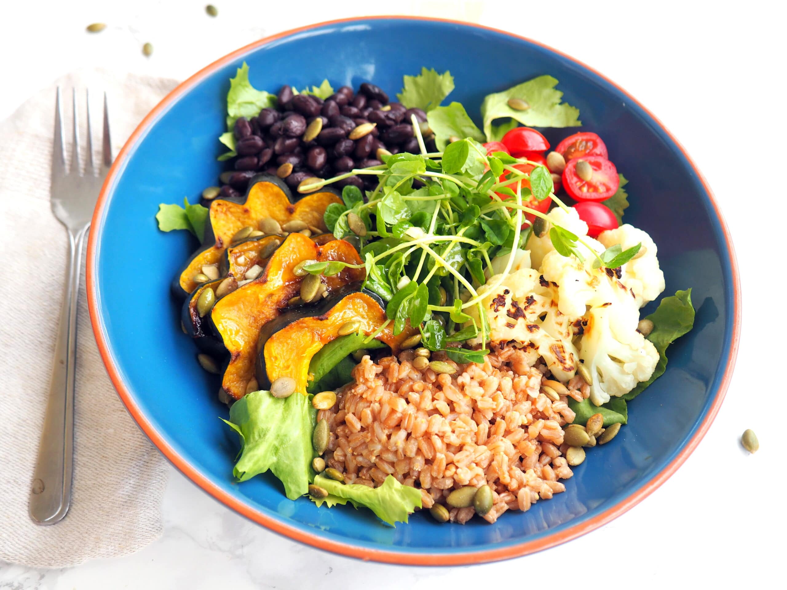 vegan power bowl featuring farro, roasted acorn squash, roasted cauliflower, black beans, grape tomatoes, pumpkin seeds, microgreens mixed greens, and a vinaigrette -- delicious, nourishing & satisfying