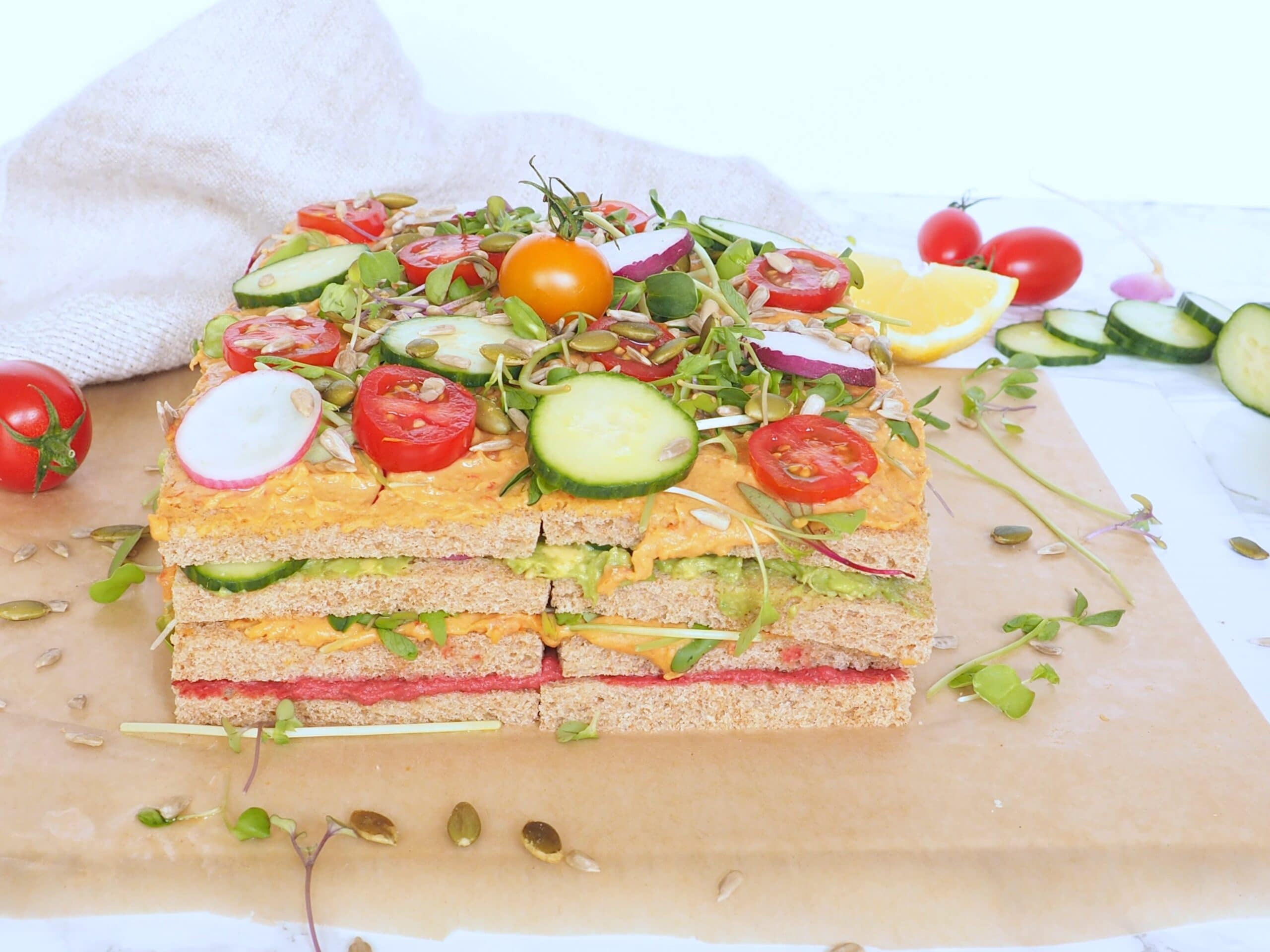 Vegan Sandwich Hummus Cake - Meet the savory hummus sandwich cake, a spin on the classic Swedish sandwich cake, it's made with layers of whole grain bread, hummus, avocado, and veggies. It's a guaranteed scene stealer at your next event and because it requires no cooking, is perfect for hot weather days. Easy to adapt to your favorite fillings and toppings. Let kids make their own version! halsanutrition.com
